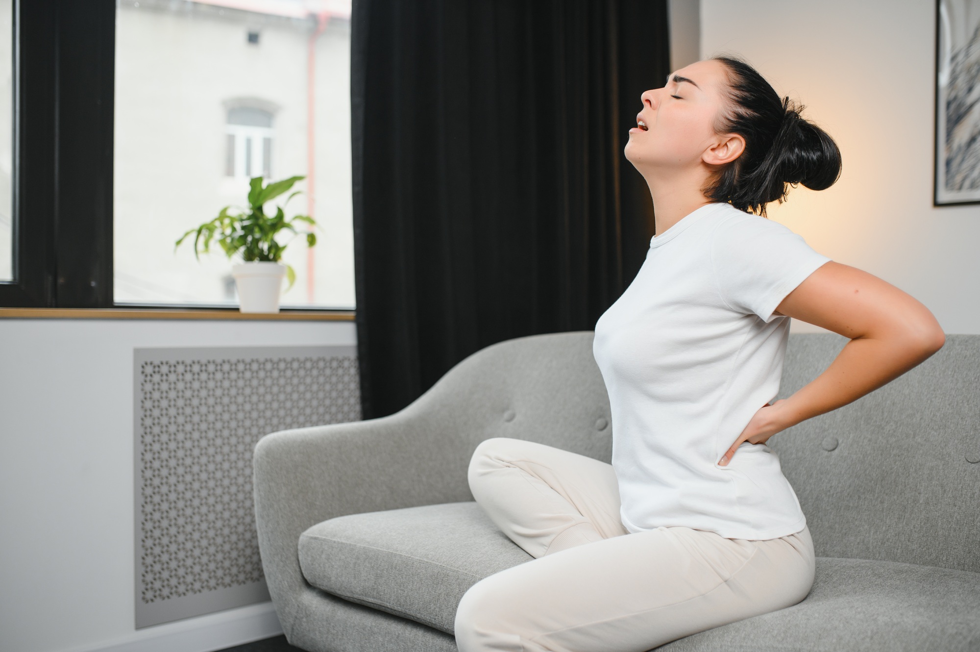 Sad young woman touching back feeling backache morning discomfort low lumbar muscular kidney pain
