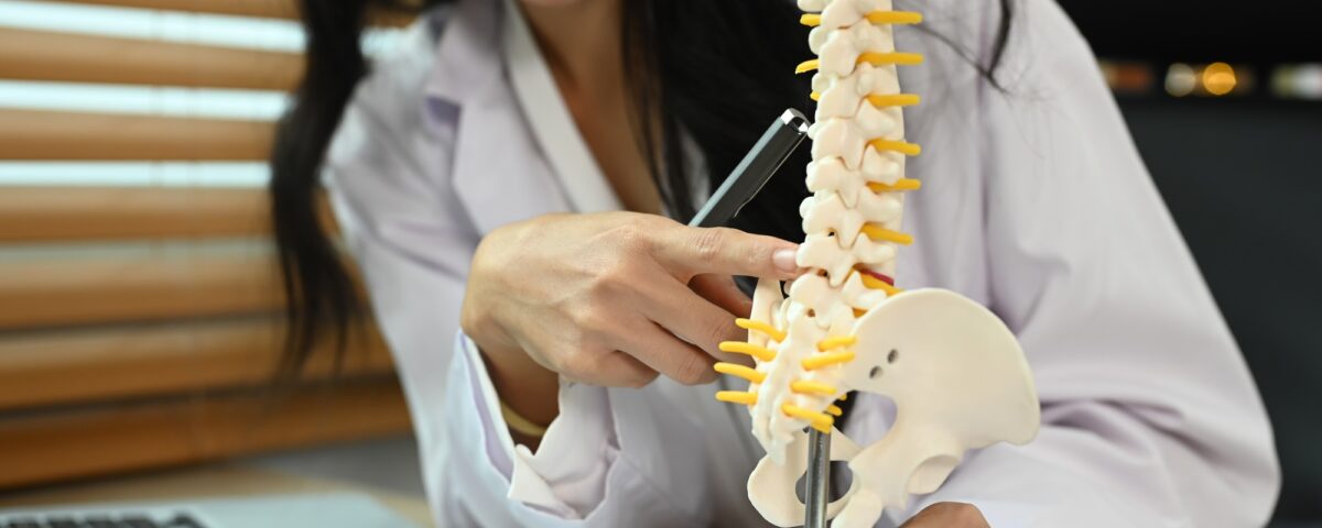 Physiotherapist showing a lumbar disc herniation with a spinal model while giving consultation.