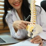 Physiotherapist showing a lumbar disc herniation with a spinal model while giving consultation.