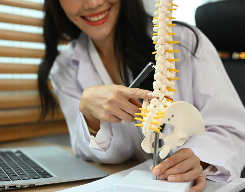 Physiotherapist showing a lumbar disc herniation with a spinal model while giving consultation.